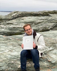 a man sitting on a rock holding up a white box