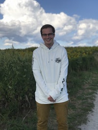 a man in a white hoodie standing on a dirt path